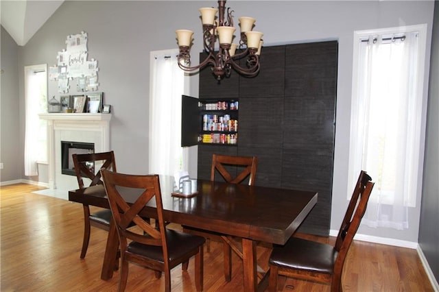 dining area with an inviting chandelier, baseboards, a fireplace with flush hearth, wood finished floors, and lofted ceiling