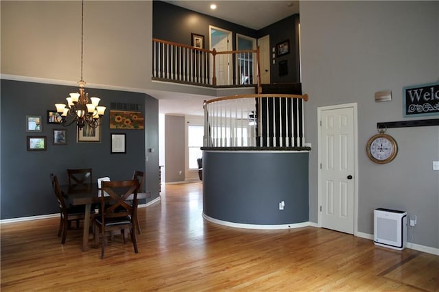 dining room featuring baseboards, a notable chandelier, wood finished floors, and a towering ceiling