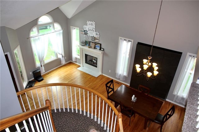 staircase featuring high vaulted ceiling, a notable chandelier, a fireplace with flush hearth, and wood finished floors