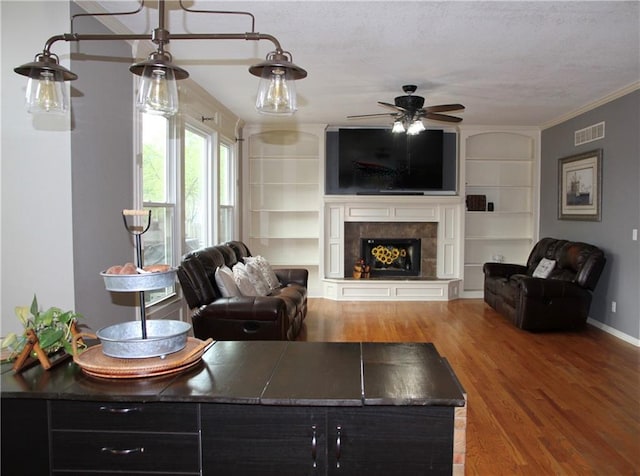 living area with a fireplace, built in shelves, a ceiling fan, wood finished floors, and visible vents
