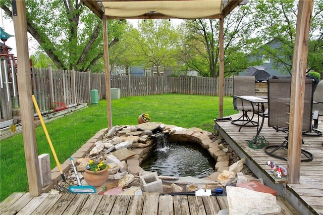 view of yard with a fenced backyard, a garden pond, a wooden deck, and outdoor dining area