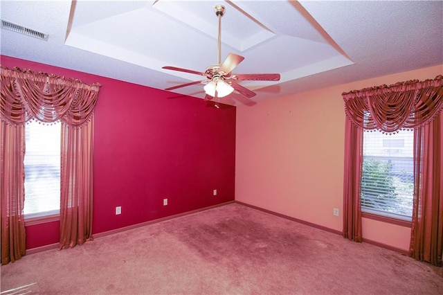 carpeted empty room with visible vents, a raised ceiling, plenty of natural light, and a ceiling fan