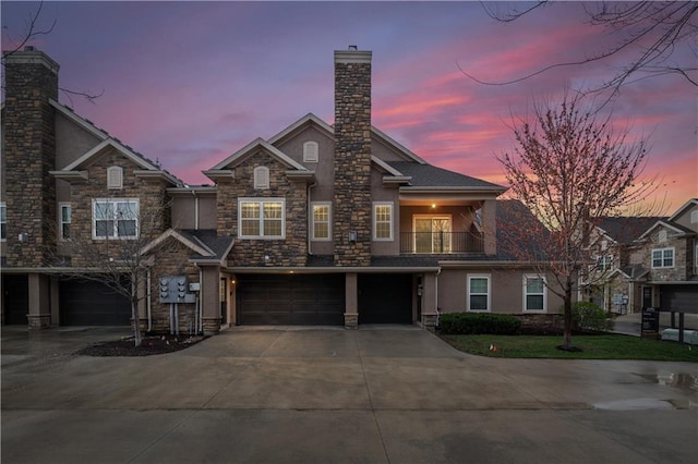 view of front of house with an attached garage, a chimney, stone siding, stucco siding, and concrete driveway