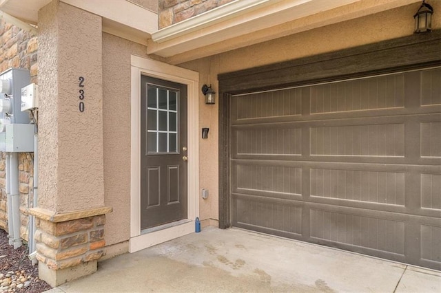 doorway to property with stucco siding, stone siding, and a garage