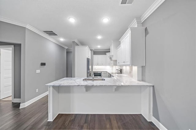 kitchen with crown molding, a peninsula, stainless steel appliances, light stone counters, and white cabinetry
