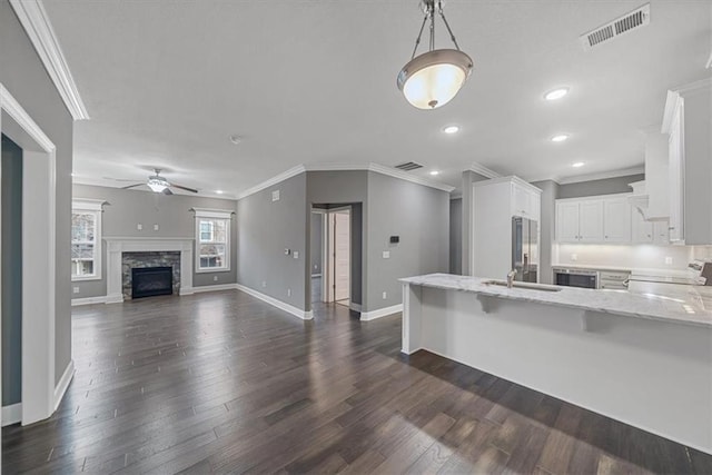 kitchen featuring ceiling fan, a peninsula, baseboards, light stone counters, and ornamental molding