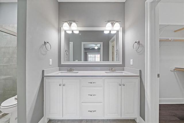 bathroom with double vanity, a spacious closet, baseboards, a ceiling fan, and toilet