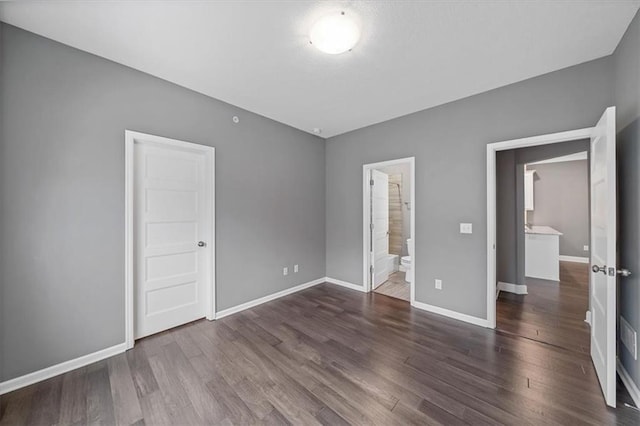 unfurnished bedroom featuring wood finished floors, baseboards, and ensuite bathroom