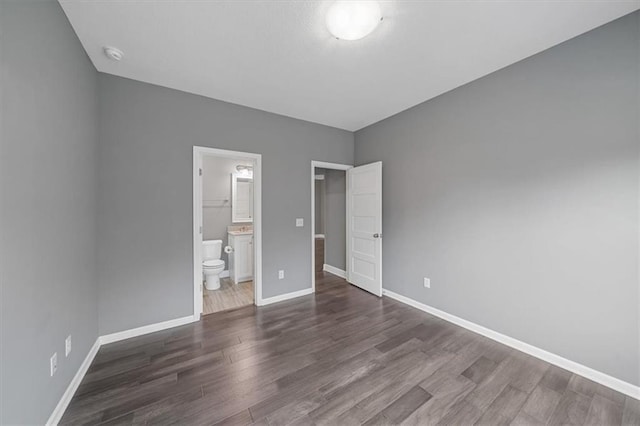 unfurnished bedroom featuring wood finished floors, baseboards, and ensuite bath