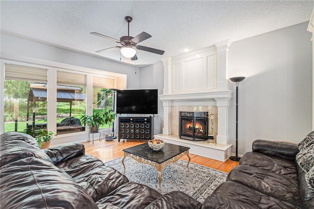 living area featuring a ceiling fan, plenty of natural light, light wood finished floors, a textured ceiling, and a fireplace