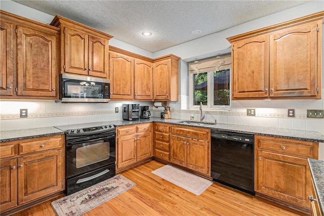 kitchen featuring black appliances, a sink, light wood-type flooring, a textured ceiling, and dark stone countertops