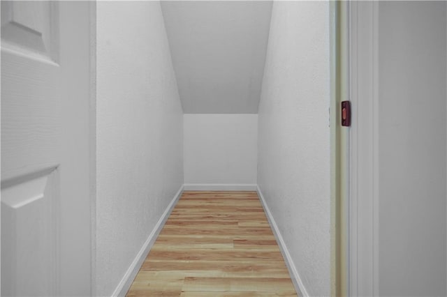 interior space featuring baseboards, a textured wall, lofted ceiling, and light wood-style flooring