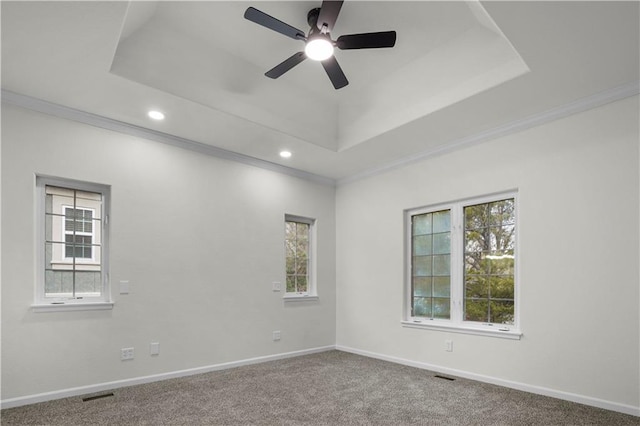 empty room featuring a tray ceiling, plenty of natural light, and visible vents