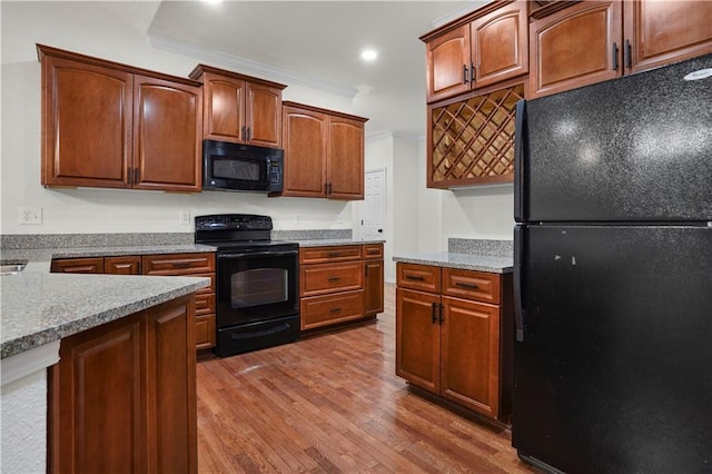 kitchen featuring light countertops, wood finished floors, crown molding, and black appliances