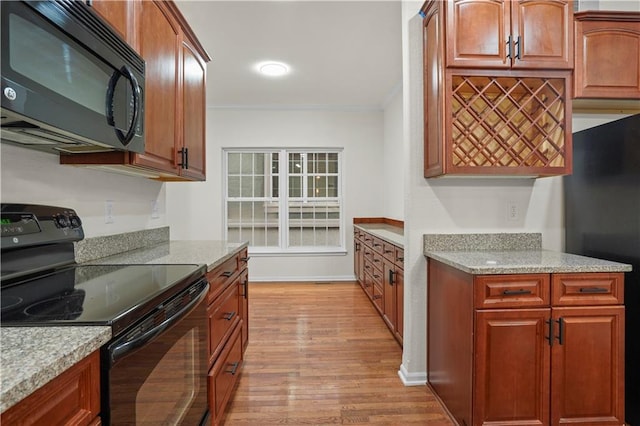 kitchen with black appliances, crown molding, light stone counters, and light wood finished floors