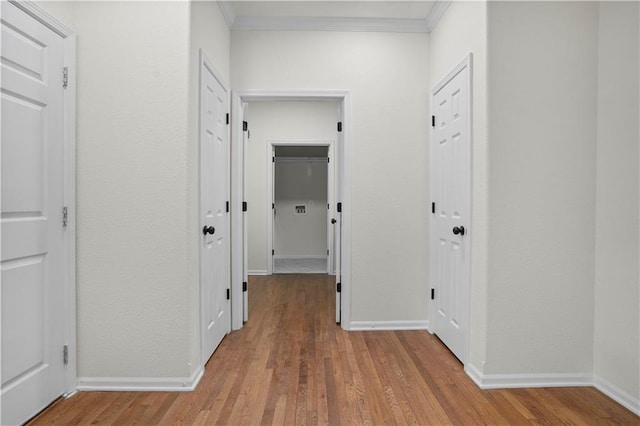 corridor featuring baseboards, wood finished floors, and ornamental molding