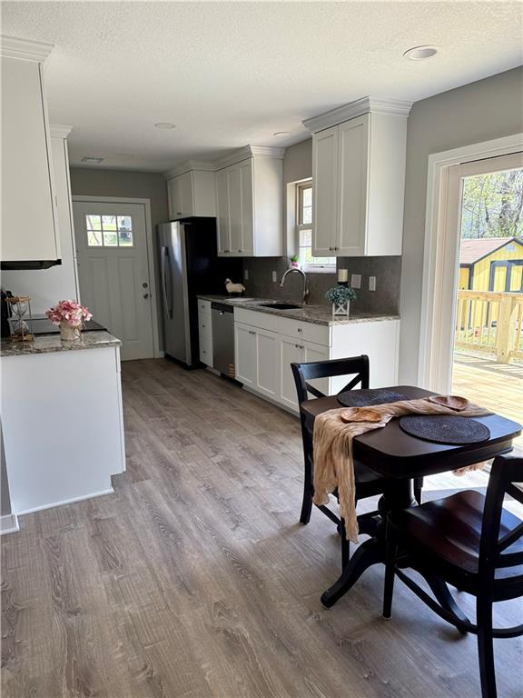 112 Benton St, Pleasant Hill, MO 64080 - kitchen featuring a sink, appliances with stainless steel finishes, light wood-style floors, white cabinetry, and decorative backsplash