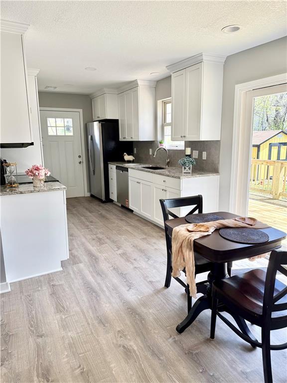 112 Benton St, Pleasant Hill, MO 64080 - kitchen with white cabinets, a sink, light wood-style floors, stainless steel appliances, and backsplash
