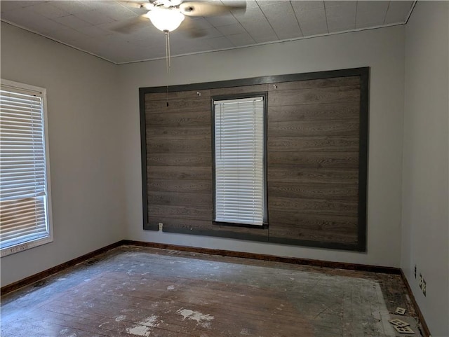 spare room featuring baseboards, wood-type flooring, ceiling fan, and a wealth of natural light