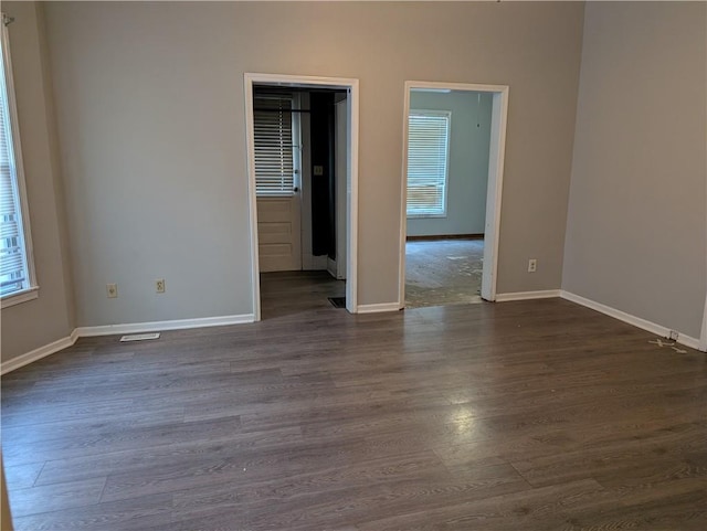 unfurnished room with baseboards, visible vents, and dark wood-type flooring