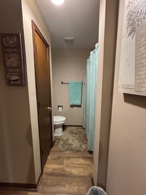 full bath featuring toilet, a shower with shower curtain, baseboards, and wood finished floors