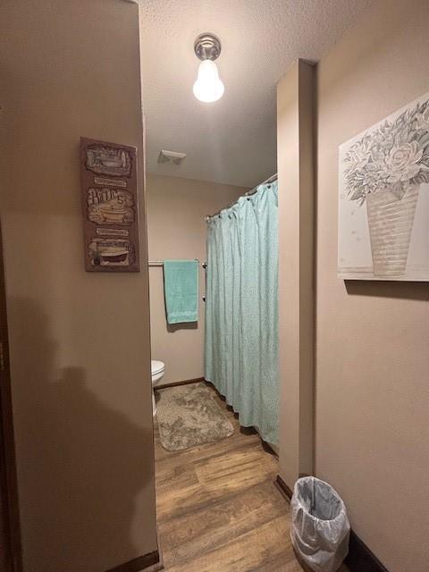 bathroom featuring toilet, curtained shower, wood finished floors, a textured ceiling, and visible vents