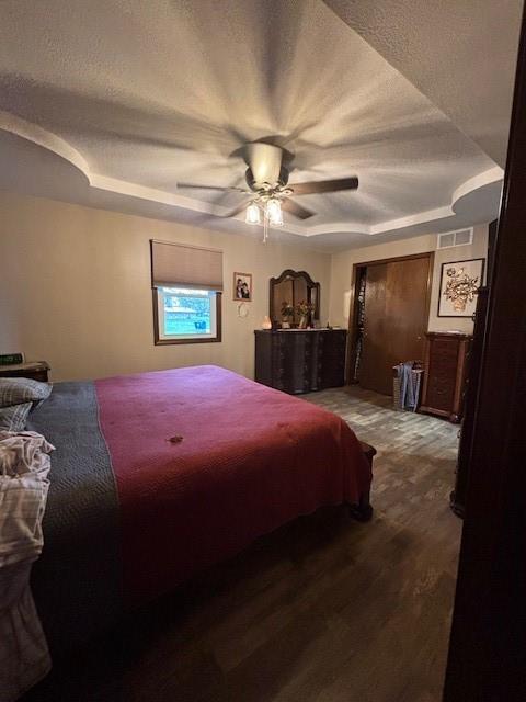 bedroom featuring dark wood-type flooring, a textured ceiling, visible vents, and ceiling fan