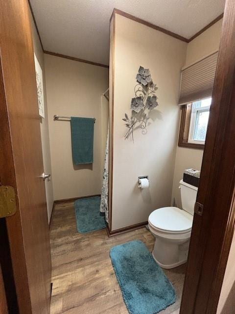 bathroom featuring a shower with curtain, toilet, ornamental molding, baseboards, and wood finished floors