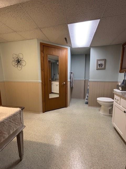 bathroom with a wainscoted wall, toilet, wood walls, and a paneled ceiling