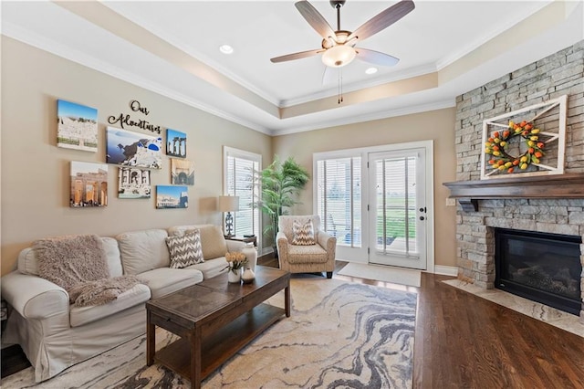 11481 S Waterford Dr, Olathe, KS 66061 - living room featuring ornamental molding, wood finished floors, a stone fireplace, a tray ceiling, and a ceiling fan