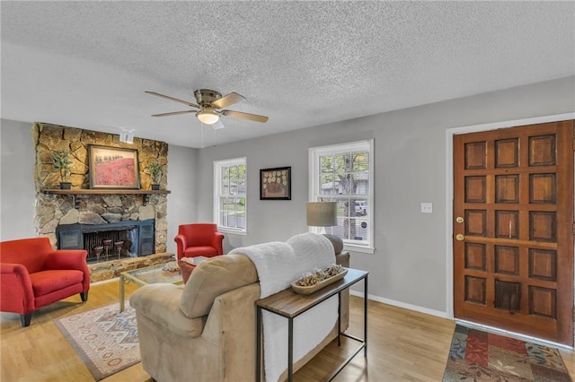 living room featuring a fireplace, a ceiling fan, baseboards, a textured ceiling, and wood finished floors