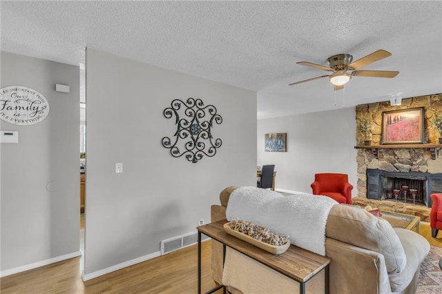 living area with a fireplace, a ceiling fan, visible vents, a textured ceiling, and wood finished floors