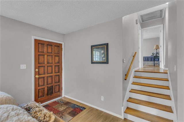 entrance foyer featuring a textured ceiling, visible vents, baseboards, wood finished floors, and stairs