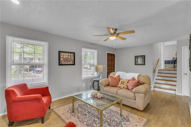 living room with a textured ceiling, ceiling fan, baseboards, wood finished floors, and stairs