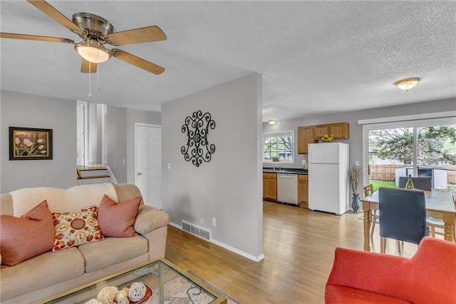 living area with visible vents, a ceiling fan, a textured ceiling, and light wood finished floors