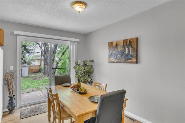 dining area featuring a textured ceiling, visible vents, baseboards, and light wood-type flooring
