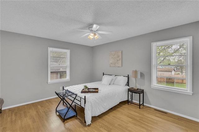 bedroom featuring a textured ceiling, a ceiling fan, baseboards, and light wood-style floors