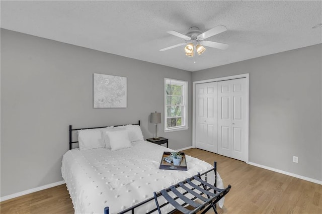 bedroom with a textured ceiling, ceiling fan, a closet, baseboards, and wood finished floors
