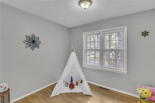 rec room featuring baseboards, visible vents, wood finished floors, and a textured ceiling
