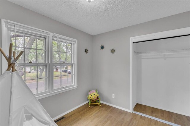 unfurnished bedroom featuring a textured ceiling, baseboards, light wood-style flooring, and a closet