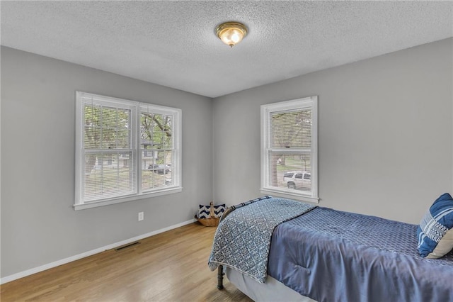 bedroom with a textured ceiling, wood finished floors, visible vents, and baseboards