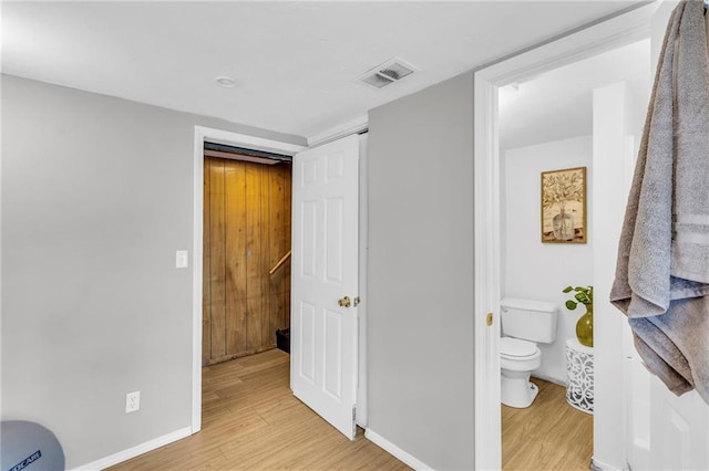 bedroom featuring baseboards, visible vents, ensuite bathroom, and light wood finished floors