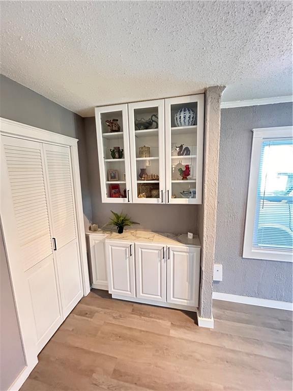 7940 Hickman Mills Dr, Kansas City, MO 64132 - bar featuring a textured wall, a textured ceiling, baseboards, and light wood-type flooring