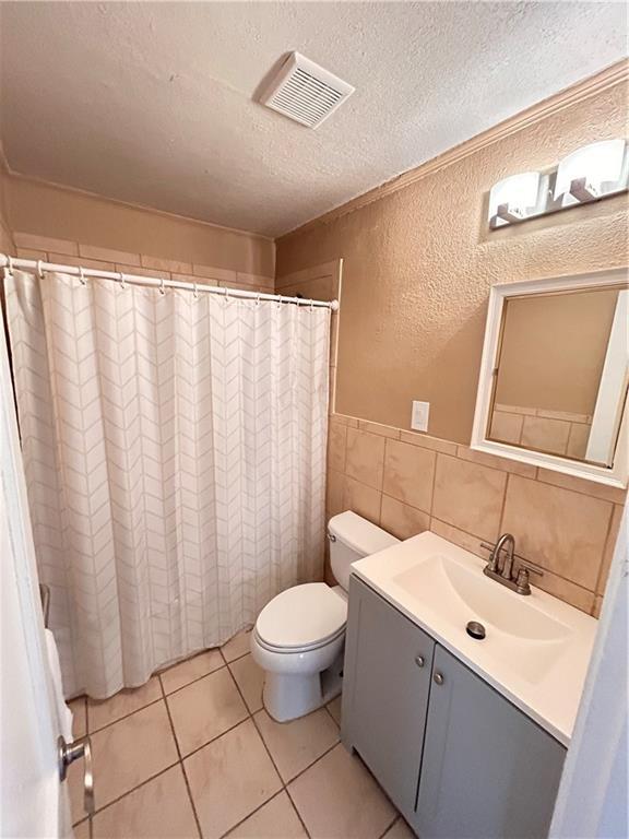 7940 Hickman Mills Dr, Kansas City, MO 64132 - bathroom with toilet, a textured wall, a textured ceiling, tile patterned floors, and visible vents