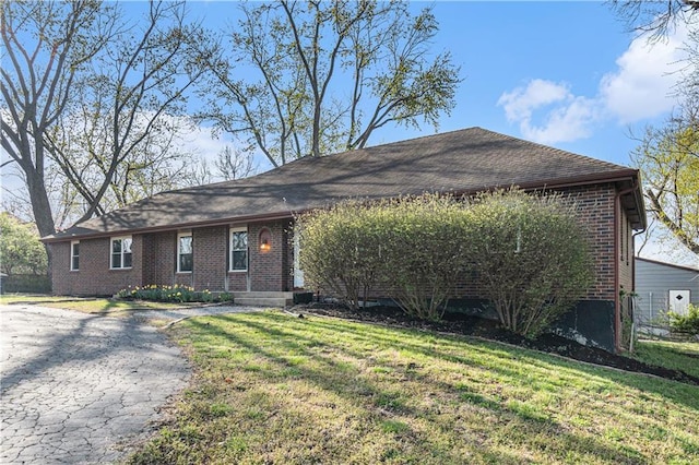 ranch-style house featuring brick siding, a front yard, and roof with shingles