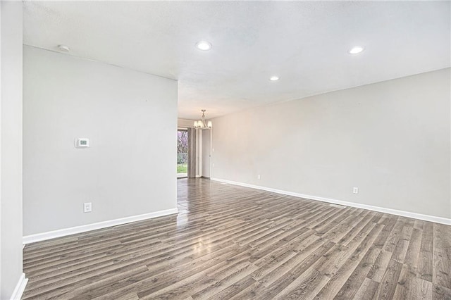 unfurnished room with baseboards, wood finished floors, recessed lighting, and a notable chandelier