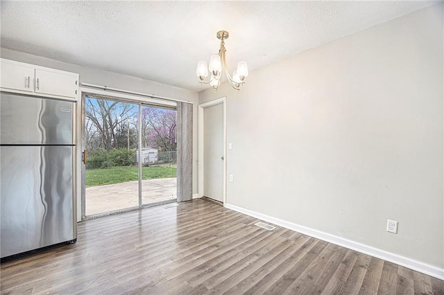 unfurnished dining area with wood finished floors, a textured ceiling, baseboards, visible vents, and an inviting chandelier