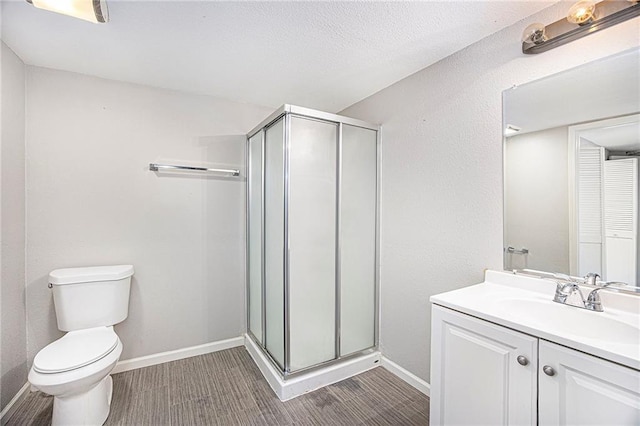 bathroom featuring toilet, vanity, a stall shower, and baseboards