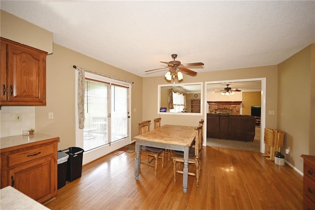 2406 NE 78th Ter, Kansas City, MO 64118 - dining space with light wood-type flooring, ceiling fan, a fireplace, and baseboards