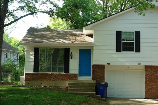 split level home with brick siding, an attached garage, cooling unit, fence, and roof with shingles